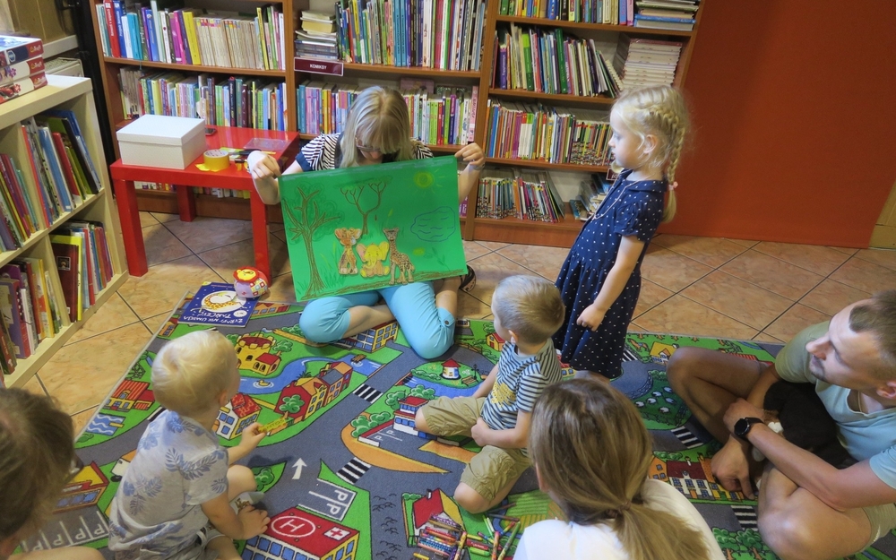 zdjęcie dzieci na dywanie z bibliotekarką prezentującą pracę plastyczną