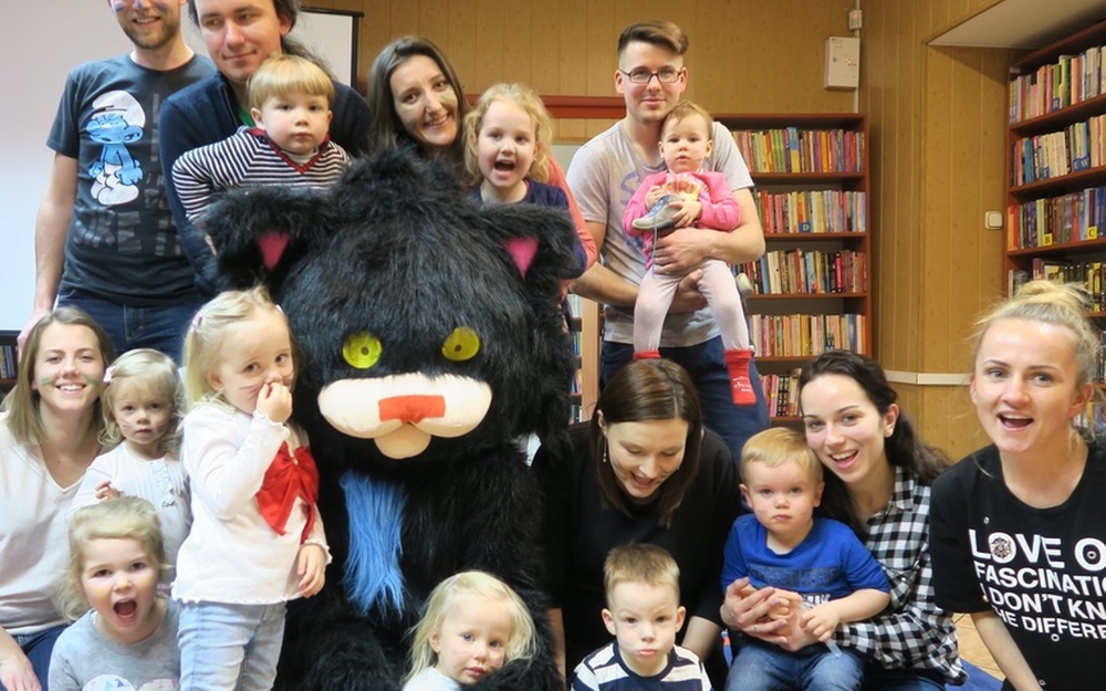 Wielki czarny, pluszowy kot w towarzystwie dzieci i dorosłych w czytelni w Długołęce 